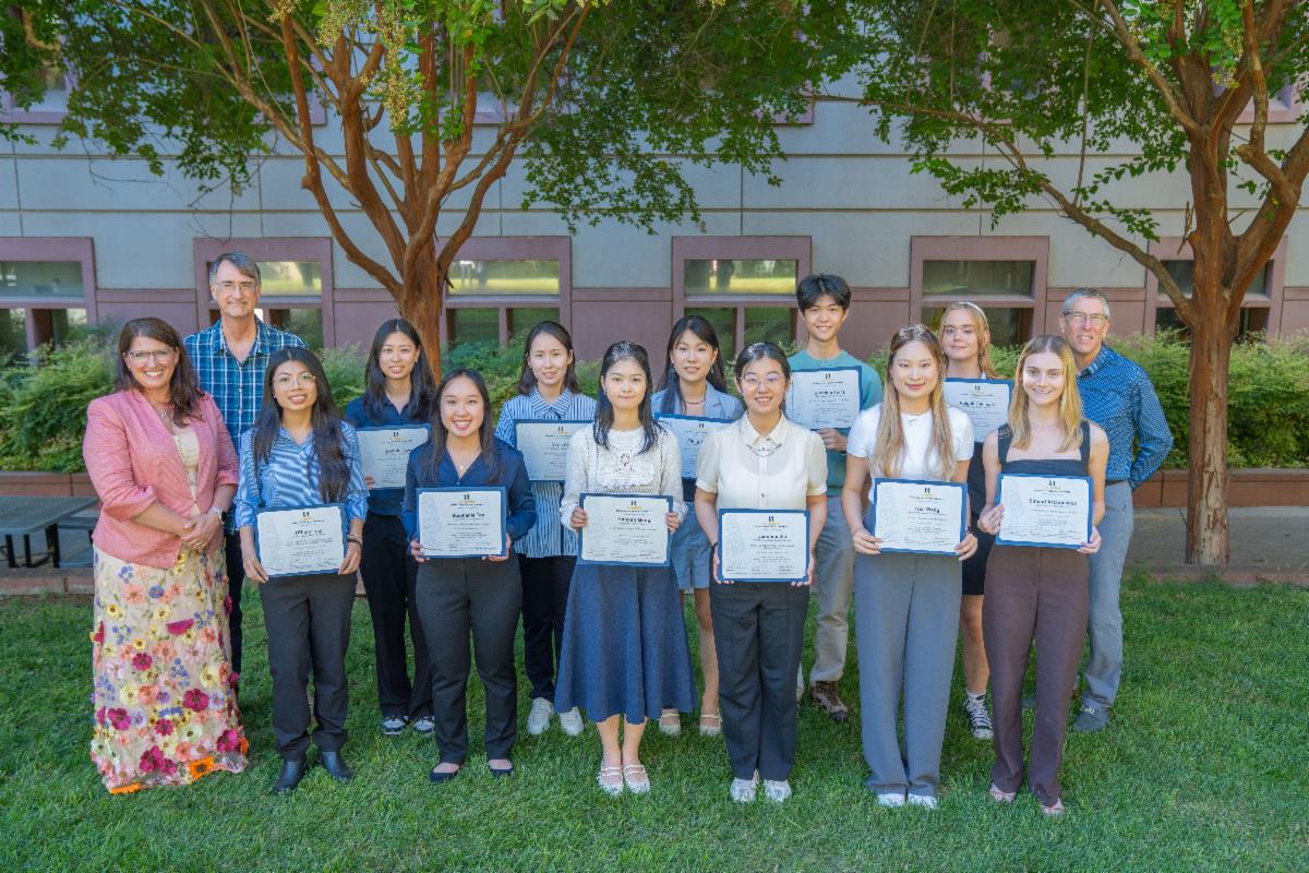 UC Davis College of Biological Sciences students from the 2025 Summer Undergraduate Research Program and program leaders standing outside holding certificates and smiling for a group photo