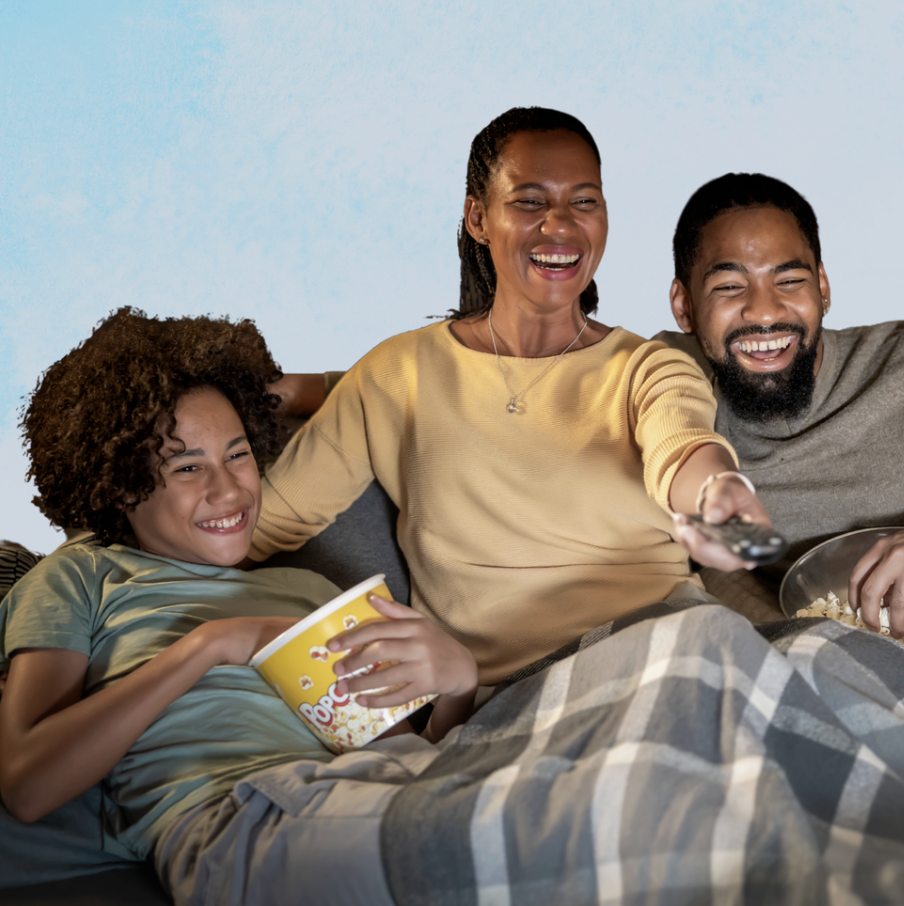 Image of a family cuddled together under a gray checkered blanket while eating popcorn and presumably watching a movie or show of some sort