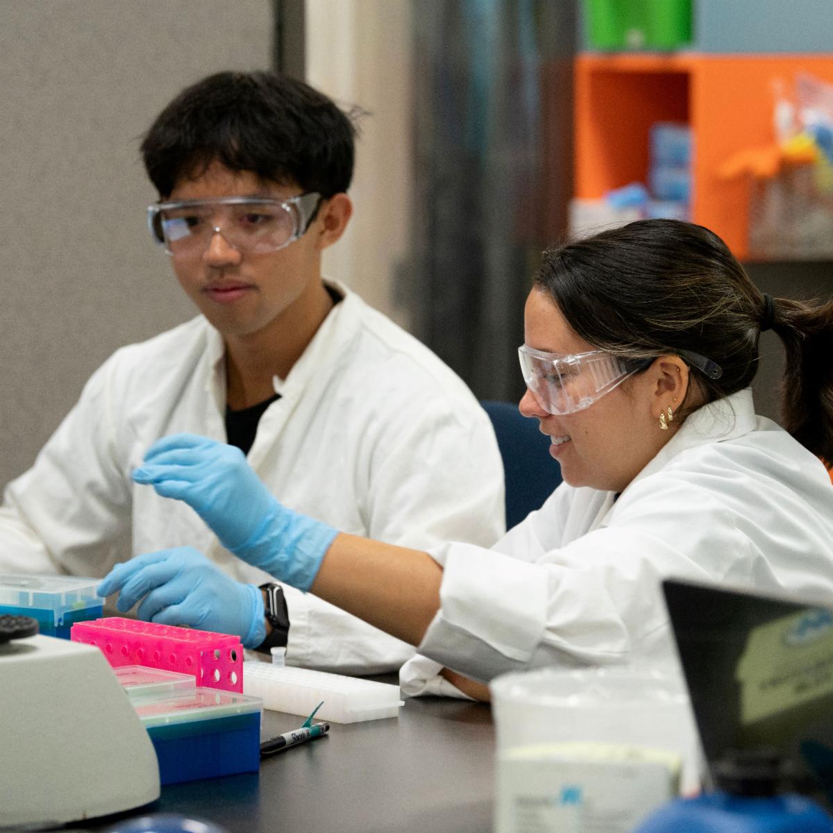 Two CBS students wearing lab coats conducting an experiment