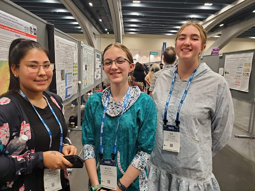 Three students stand in front of a gallery of scientific posters.