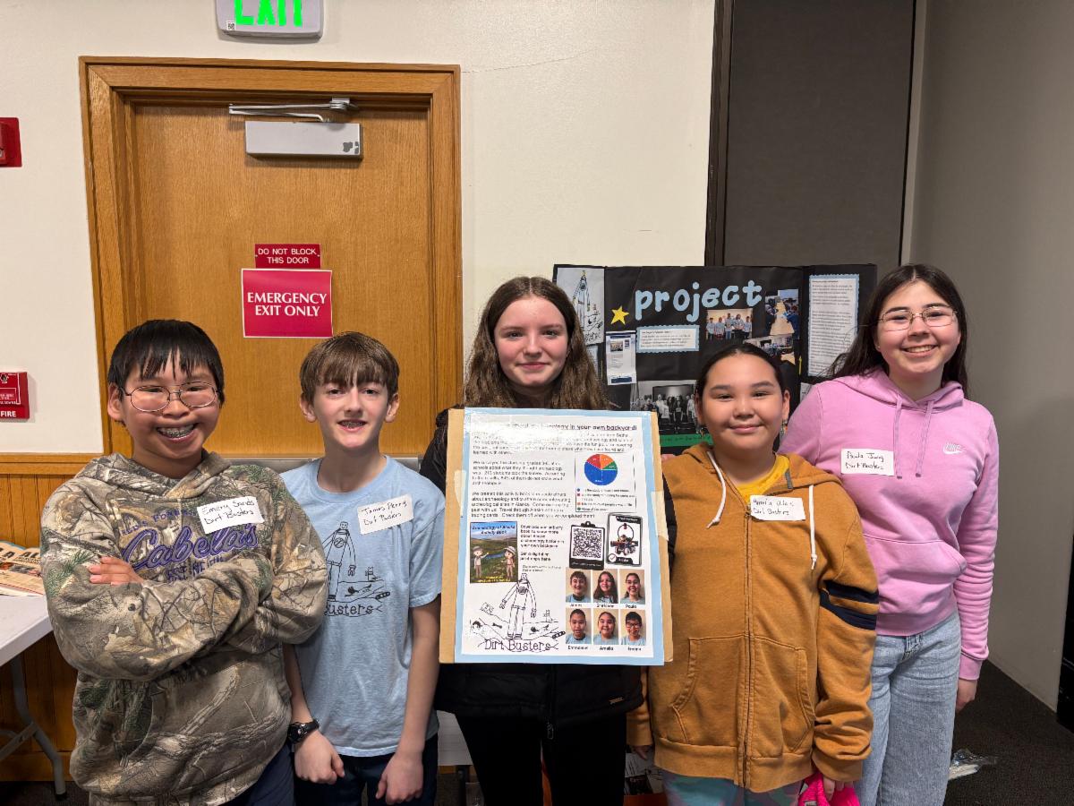 Five students smile in front of their science project poster