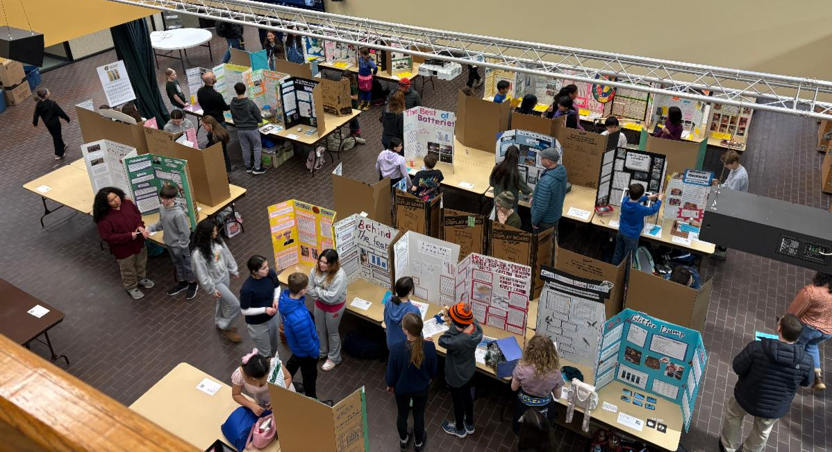 Students stand in a hall in front of tri-fold posters displaying their science projects