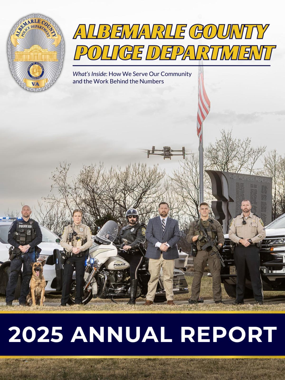 Six police officers standing in front of an American Flag with a drone in the air and a police K-9 in the forefront.