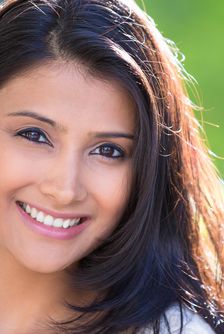 Closeup headshot portrait of confident smiling happy pretty young woman_ isolated background of blurred trees_ flowers. Positive human emotion facial expression feelings_ attitude_ perception