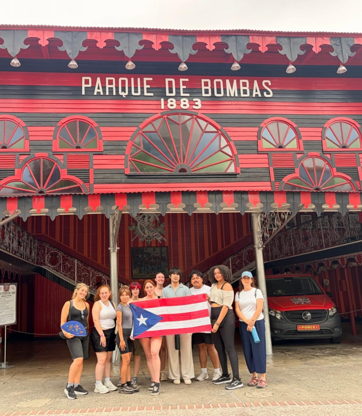 Various students holding the Puerto Rico flag standing in front of a building that says, "Parque De Bombas 1883".