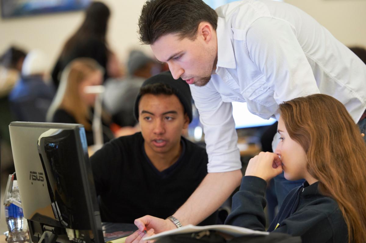 two students watching a mentor give them instruction while working on their computer