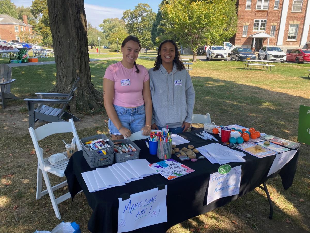 Two people at an outdoor table with art supplies at a community event
