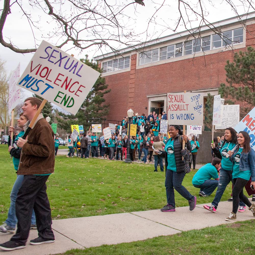 people marching to end sexual violence holding protest signs in front of a brick building