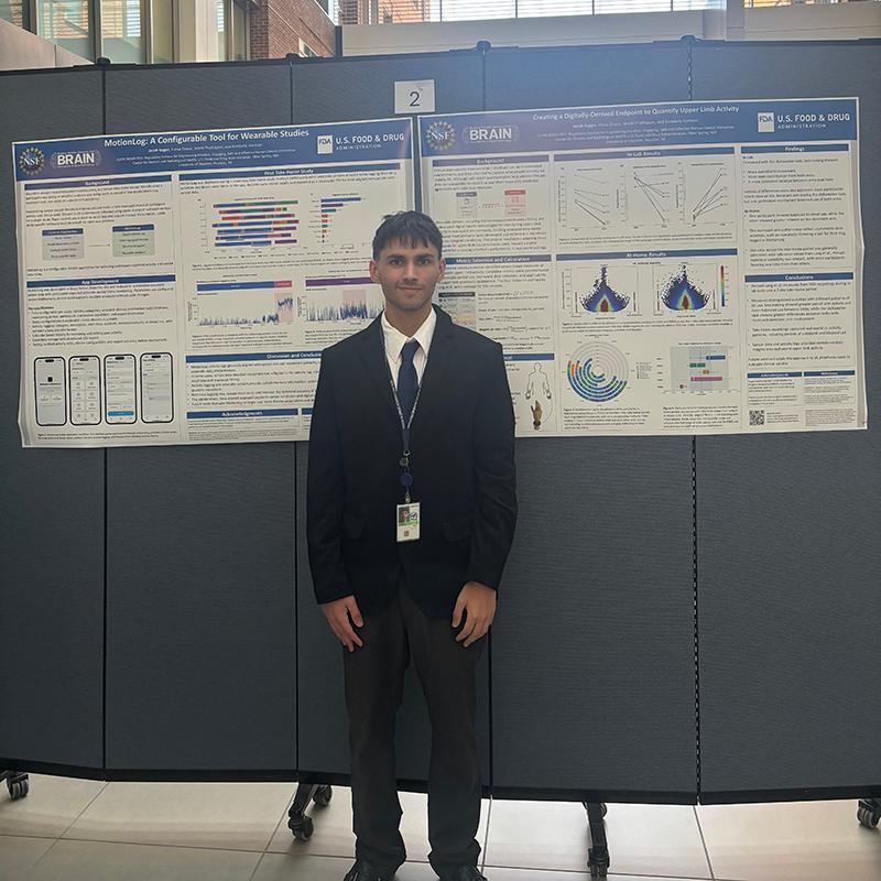 Person standing in front of two research posters about wearable activity monitoring and upper-limb movement.