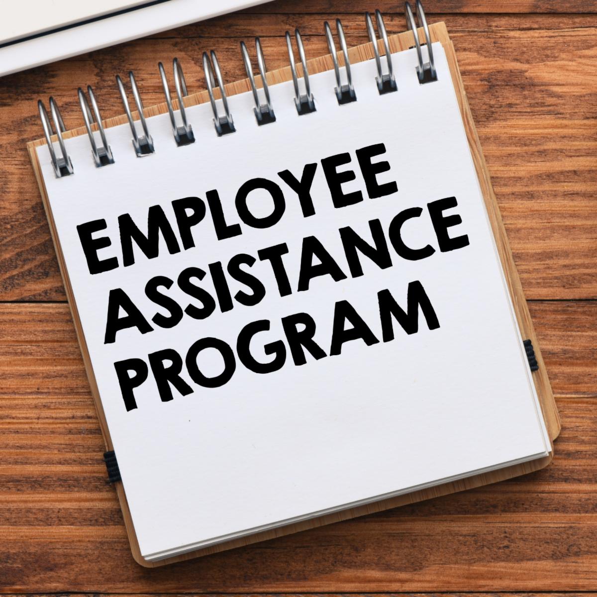 A notebook with the text EMPLOYEE ASSISTANCE PROGRAM on a wooden surface