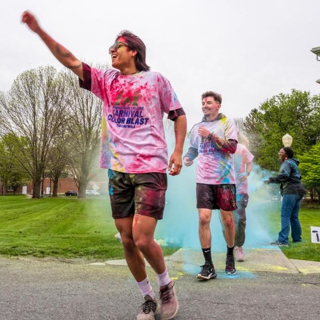 runner covered in colored powder raises arm in the air as they cross the finish line