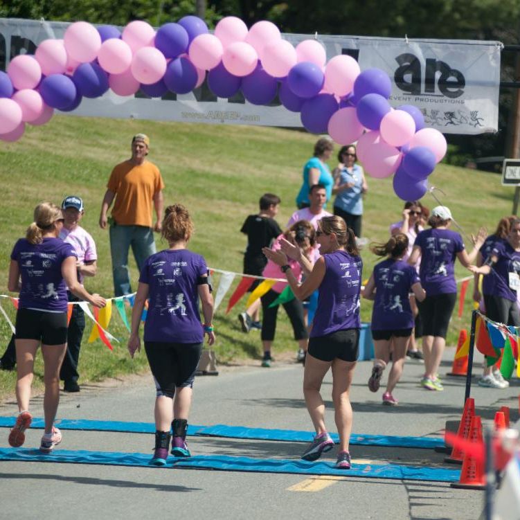 group of people crossing 5K finish line under balloon arch.