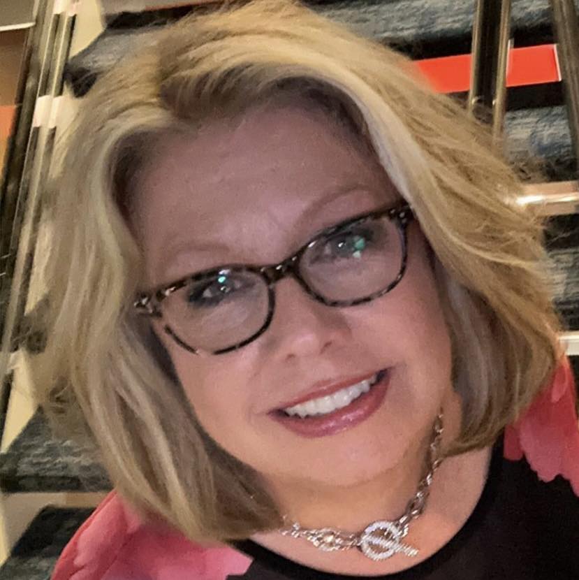 A woman with chin length blonde hair glasses and a bright smile 