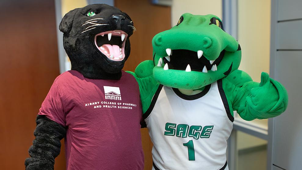 A black panther mascot and a green alligator mascot stand together in an indoor setting