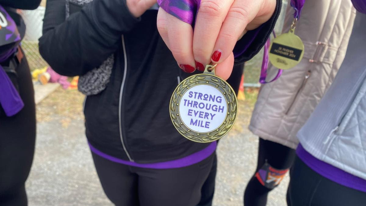 A hand holding a medal that reads STRONG THROUGH EVERY MILE