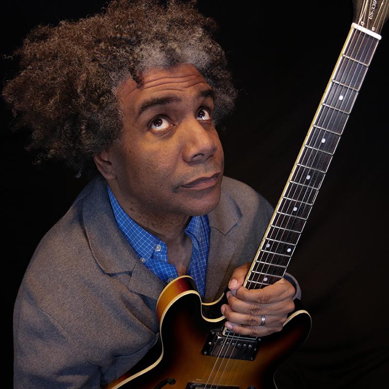 Close-up portrait of a man holding an electric guitar against a black background.