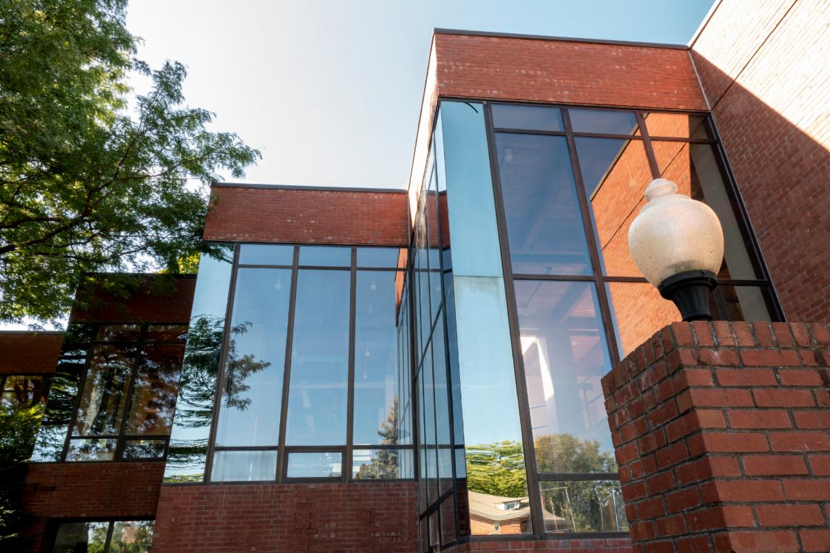 A modern building with large glass windows and red brick walls featuring a glass light fixture on a brick pillar