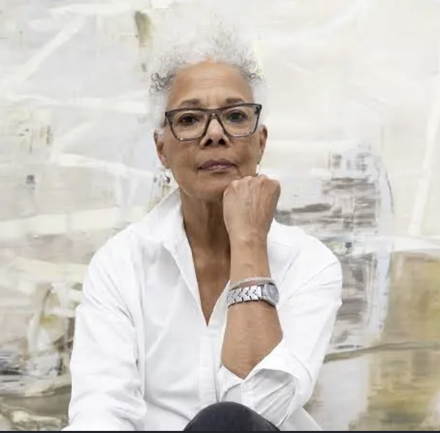 woman with short gray hair and glasses resting her chin on her hand, wearing a white shirt and silver wristwatch