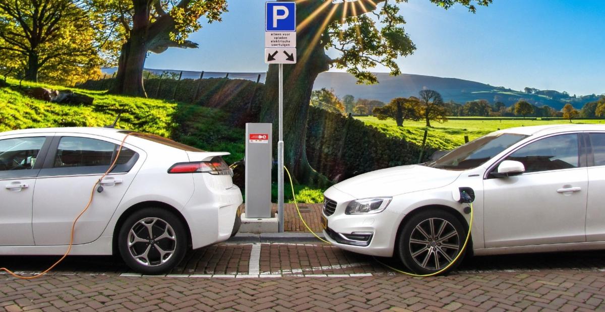 two white cars parked at a charging station with trees and mountains behind them