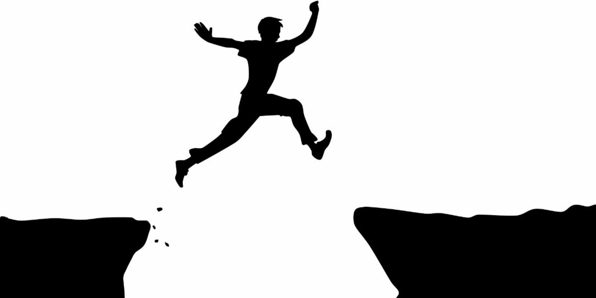 a silhouette of a man jumping over a ravine 