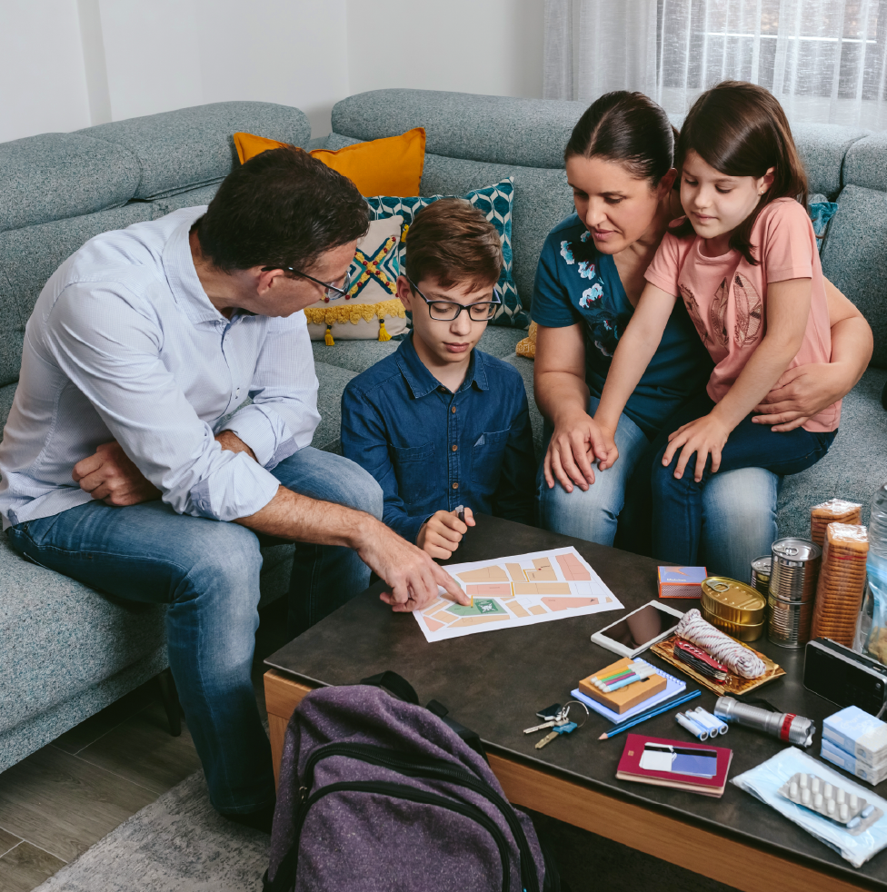 Family reviews an emergency plan at home with supplies like water, food, and a first aid kit on the table.