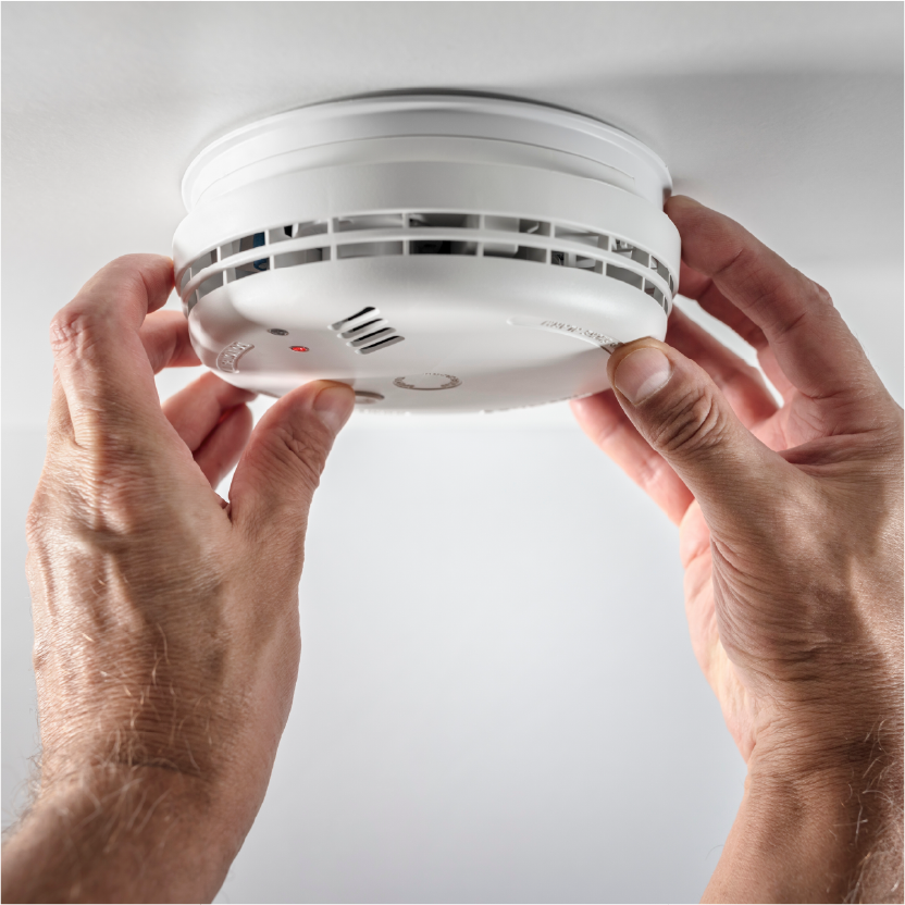 Hands reaching up to twist a smoke detector out of the ceiling. 