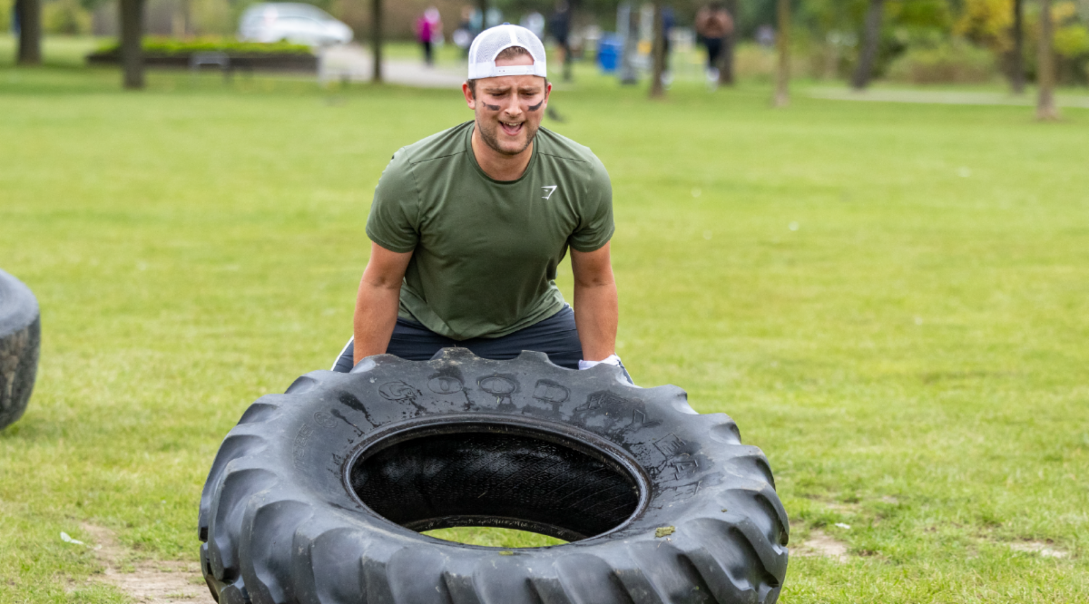Man hunched over attempting to flip over a tractor tire.
