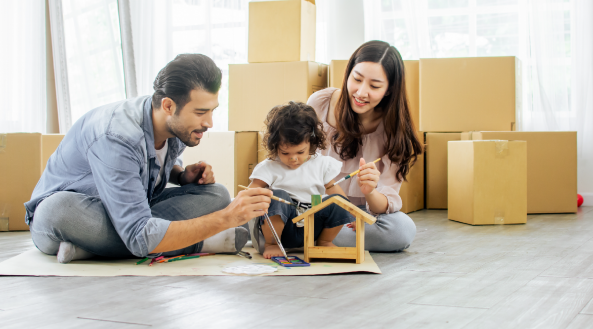 Parents playing with their toddler on the floor with boxes yet to be unpacked in the background.
