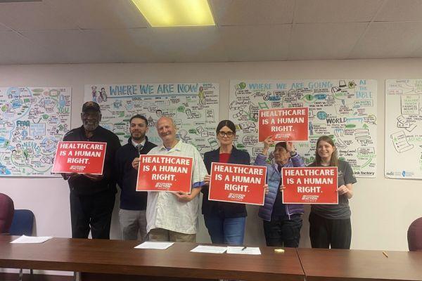 Group of people in a conference room holding signs that say Healthcare is a Human Right