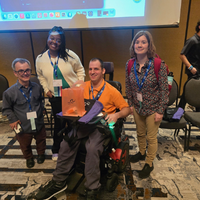 Four people in a hotel meeting room assembled together for a picture 