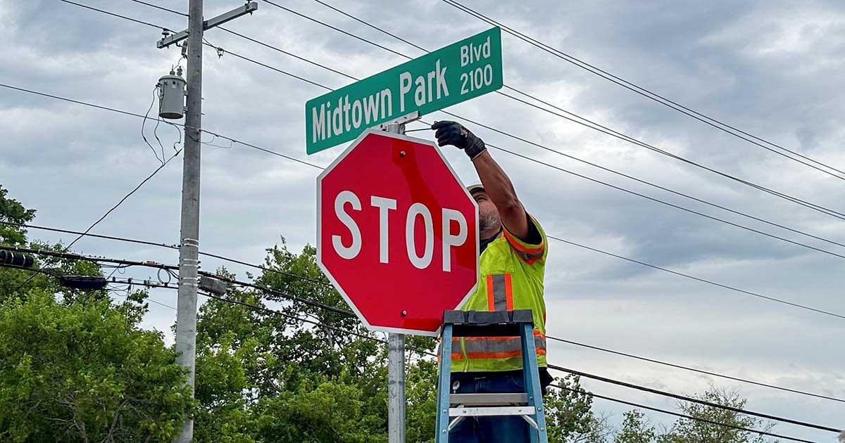 City employee attaches Midtown Park Boulevard sign to the top of a stop sign post.