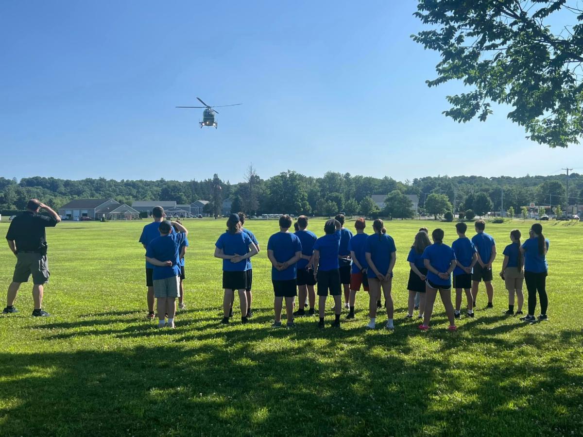 A group of people standing on a field watching the the Life Flight helicopter in the air.