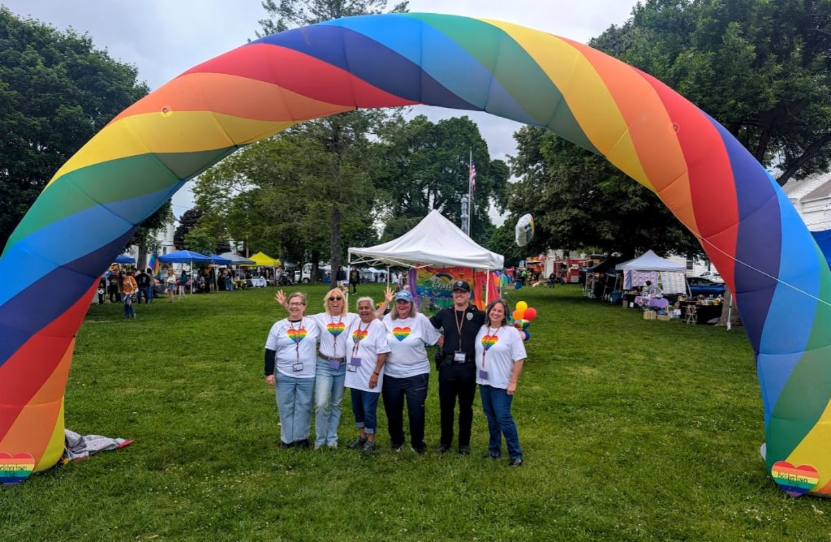 A group of people on the Town Common posing for a picture under the rainbow arch during the Pride event.