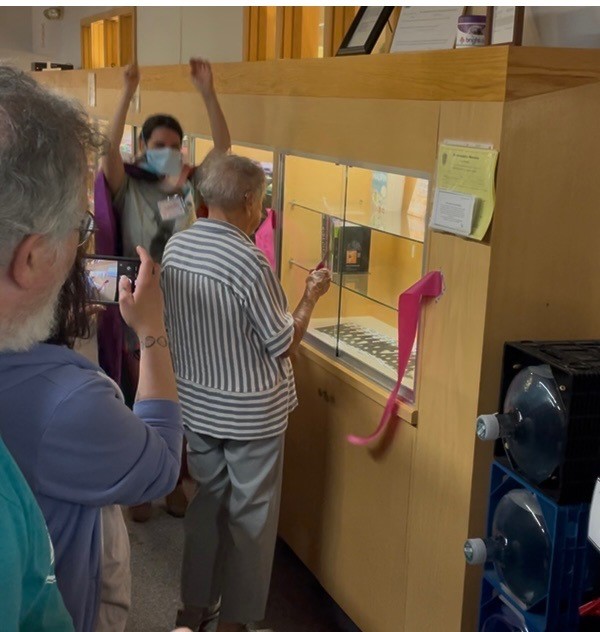 People surrounding the new bookshelf during the opening ceremony showing a ribbon that was jut cut