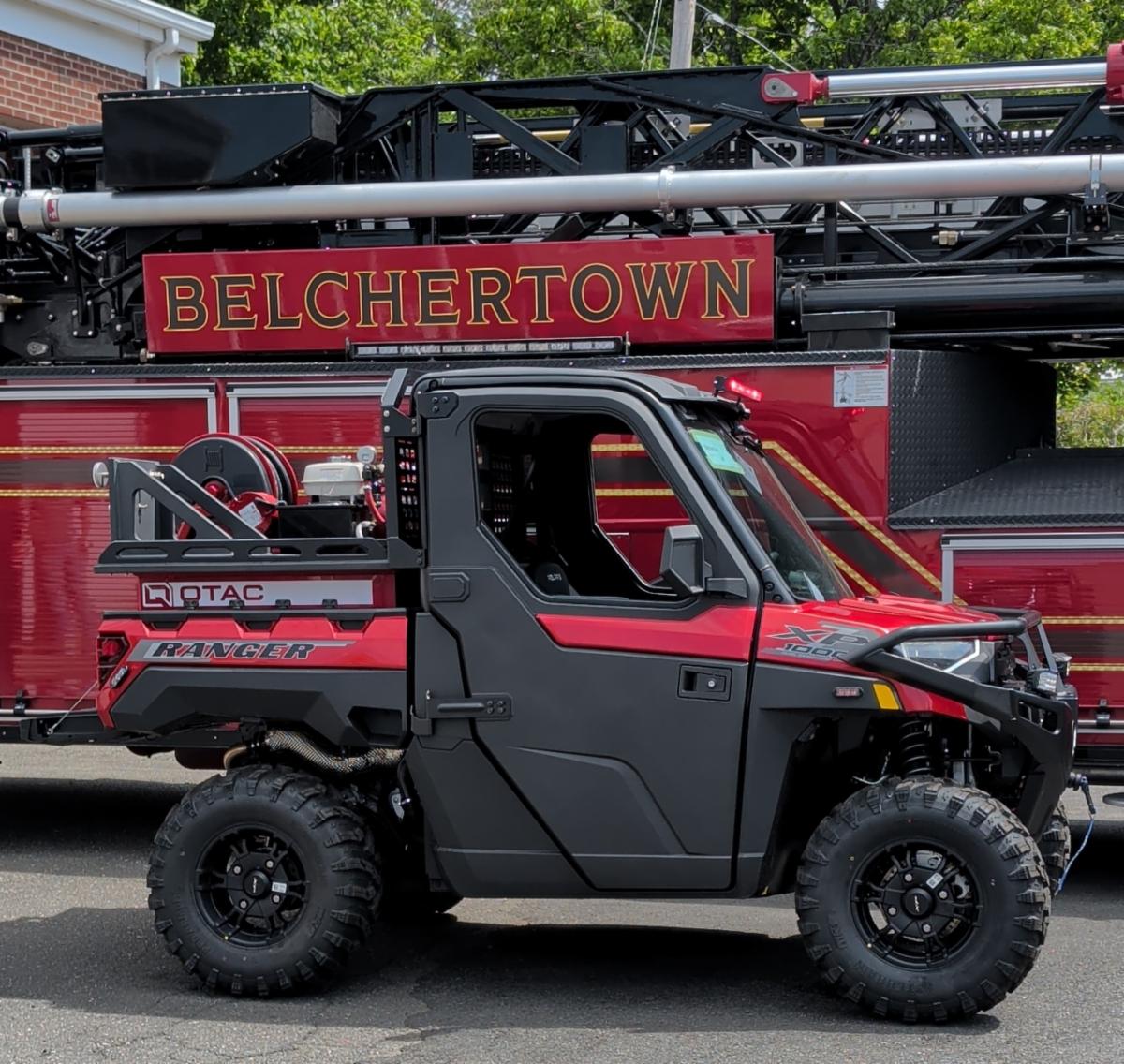 A red Polaris Ranger XP 1000 utility terrain vehicle (UTV) outfitted with QTAC fire and rescue equipment, parked in front of a Belchertown fire truck.
