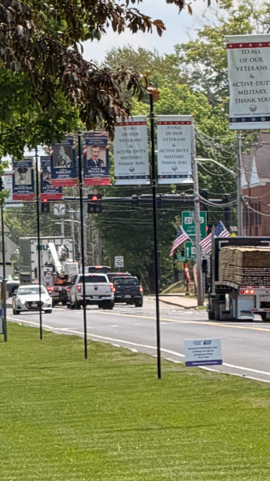 A Belchertown street lined with military honor banners on lamp poles, with a large sign reading 'To All of Our Veterans 