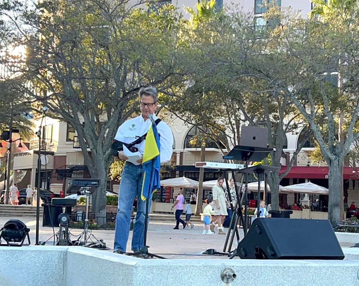 County Commissioner Gregg Weiss outdoors speaking on stage with Ukrainian flag showing