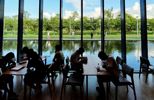 Students studying at tables before large window and water