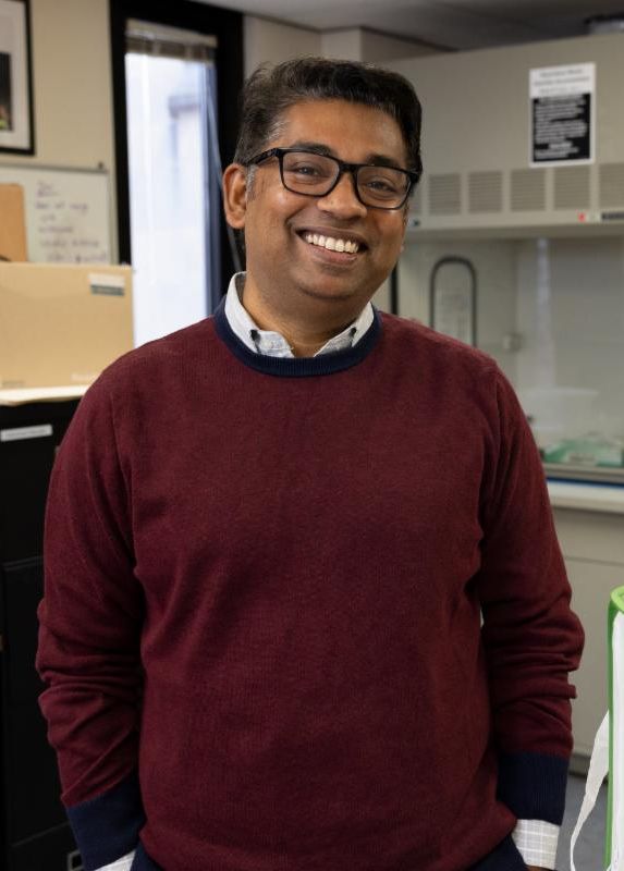 Rupesh Kariyat wearing glasses and a red sweather smiles warmly at the camera.