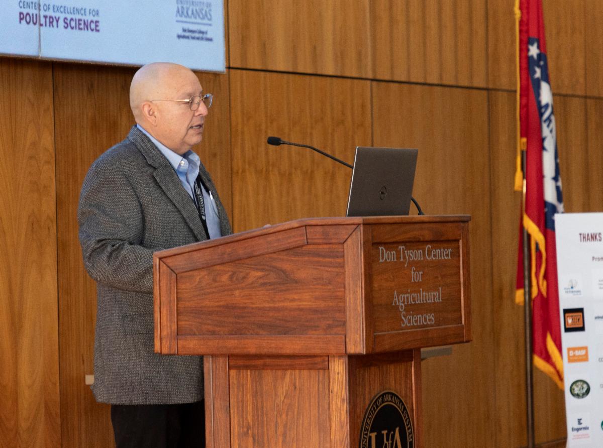 A man stands and speaks from a podium with a screen in the background