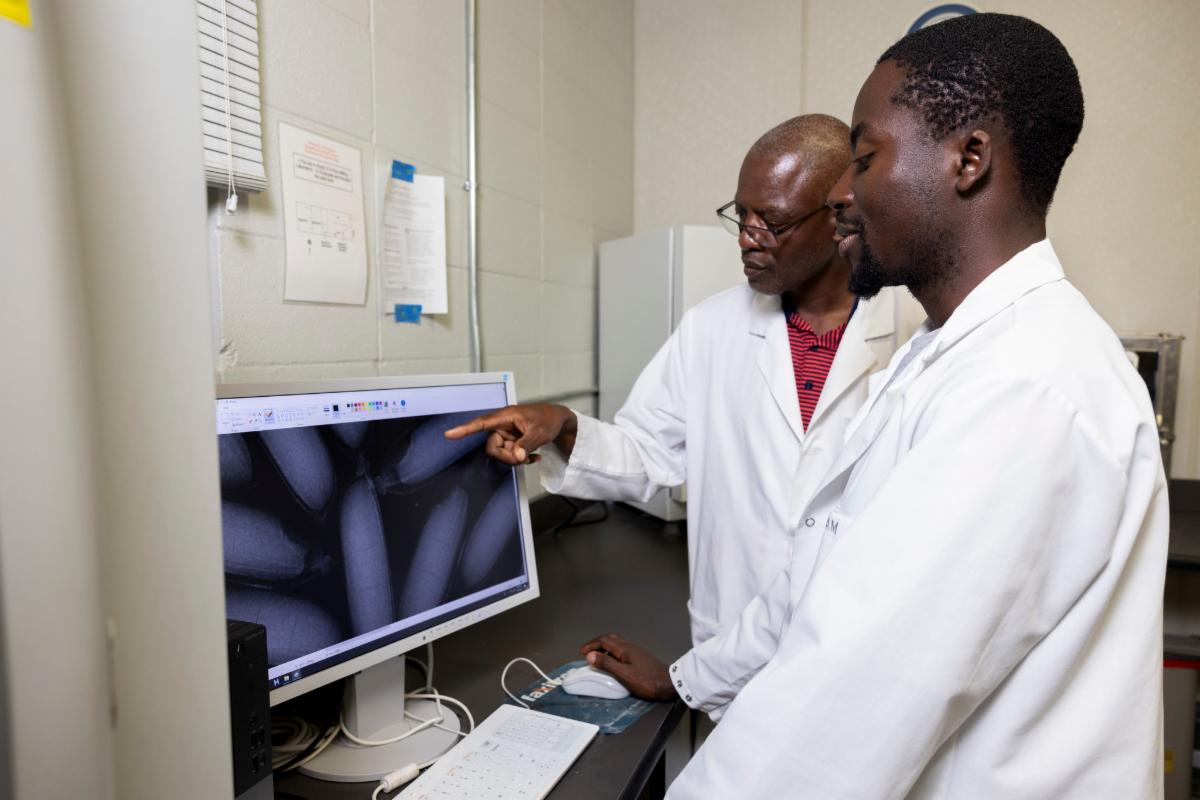 Two men in lab coats standing beside a computer, engaged in discussion or analysis.