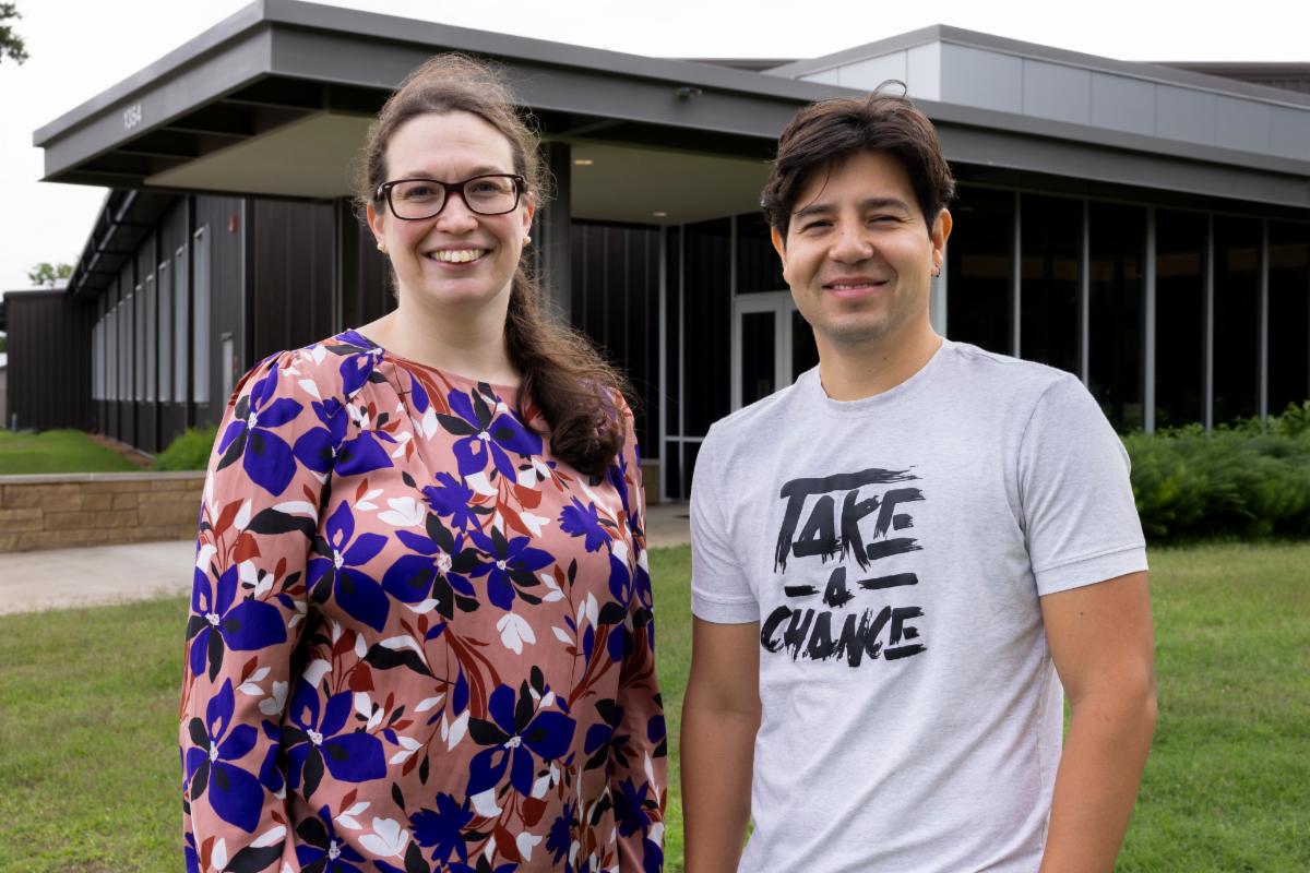 Aurelie Poncet and Mario Andres Soto Valencia stand beside a green plant, smiling and engaged in conversation.
