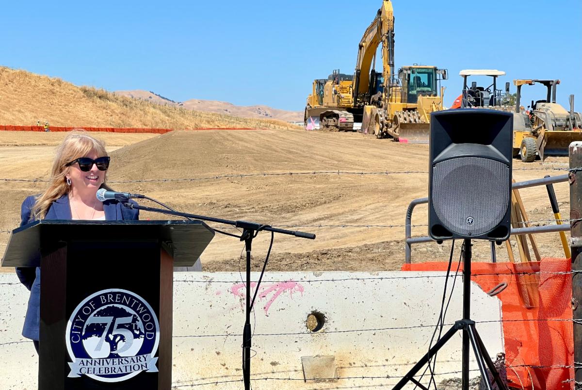 Supervisor Burgis speaks in front of construction equipment at the groundbreaking ceremony on Sand Creek Road