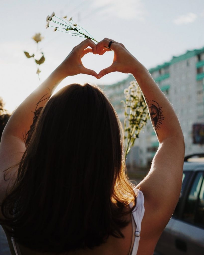 A young woman is outside, holding her hands in the shape of a heart