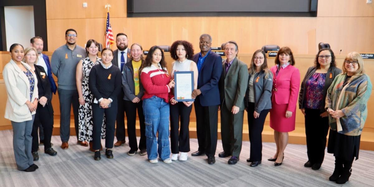 16 people, including Supervisor Burgis, pose for a photo in the Board chambers