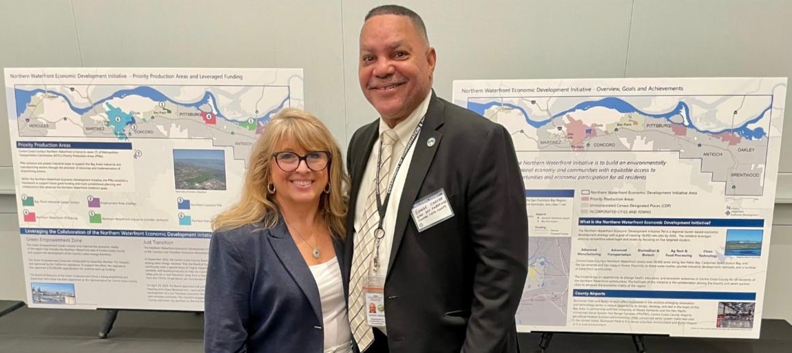 Supervisor Burgis and George Carter stand in front of posters for the Northern Waterfront Economic Development Initiative