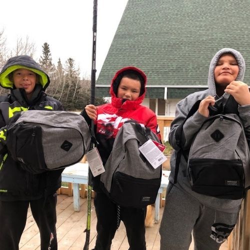 Three Indigenous students standing outside holding new backpacks.