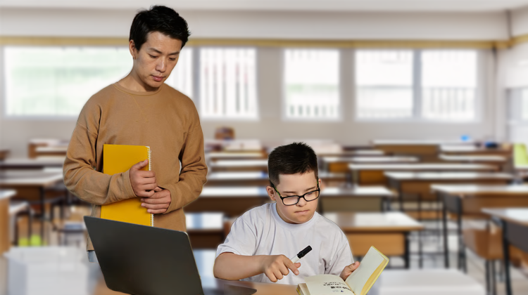 A student wearing glasses works at a desk with books and a laptop while an adult stands nearby holding a notebook.