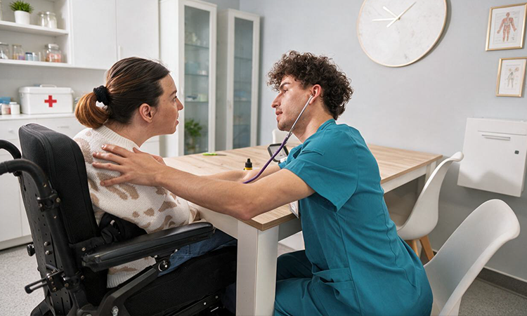 A healthcare worker uses a stethoscope to examine a woman seated in a wheelchair.