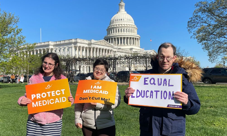 Three people stand in front of the US Capitol holding signs supporting Medicaid and equal education